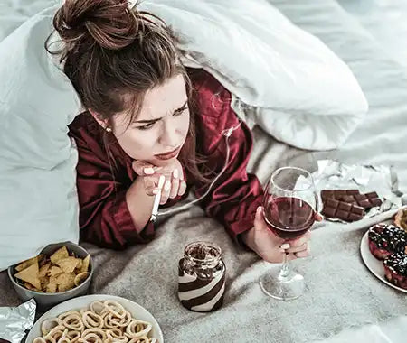 Frau im Bett mit Zigarette, Wein und Fast Food