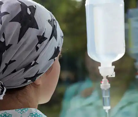 Person von hinten mit Tropf wegen Haarausfall durch Chemotherapie